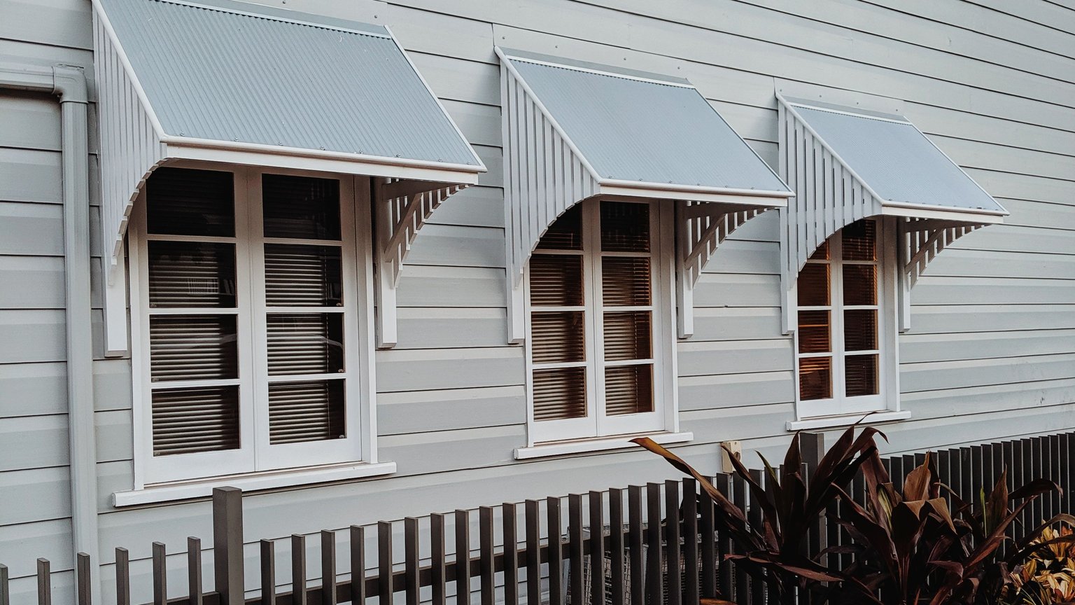 Weatherboard Queenslander in New Farm, Brisbane, with corrugated iron window hoods above a slatted front fence